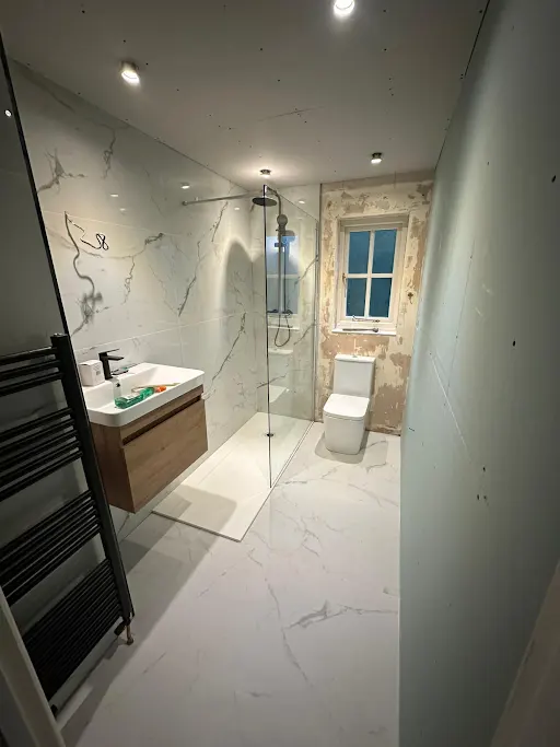 Marble-tiled wet room with walk-in shower, wall-hung basin and black towel radiator
