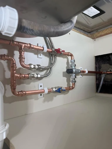 New isolation valves and copper pipework under a kitchen sink